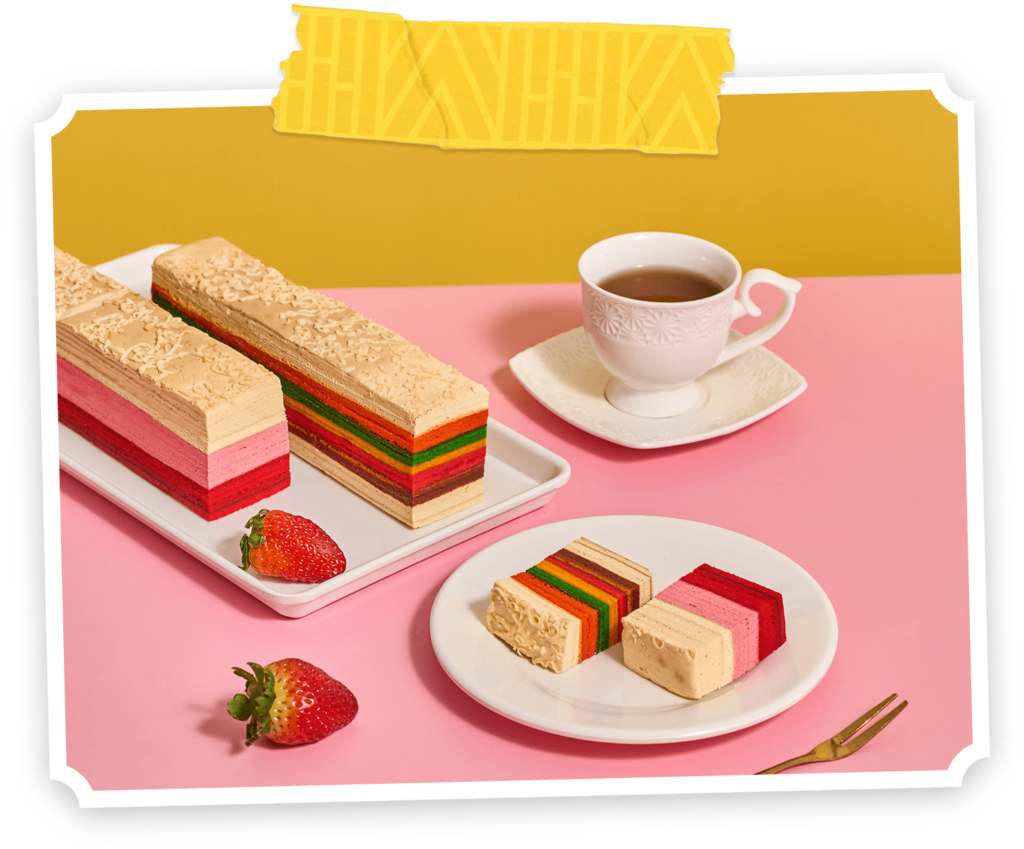 Strawberry & Cheese Ice Cream layered cakes with colorful stripes are presented on a white tray and white plate, accompanied by fresh strawberries and a cup of tea at the side